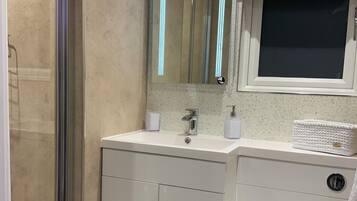 A modern bathroom with a glass shower enclosure, a white sink with a mirror above, and a toilet.