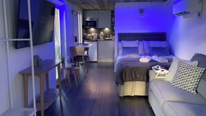 A modern bedroom with a bed, a sofa, a TV, a desk, and a kitchen area. - Royal Snug & WEE Snug (Aboyne)
