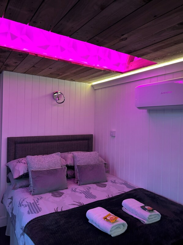 Een slaapkamer met een bed, kussens, een nachtkastje en een wandairconditioner.