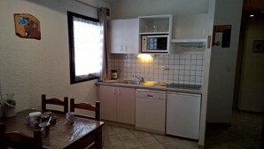 A compact kitchen with white cabinets, a microwave, and a sink. There is a dining table with chairs and a window with curtains.