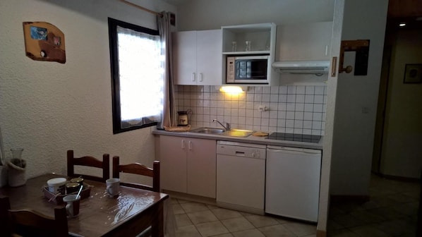 A compact kitchen with white cabinets, a microwave, and a sink. There is a dining table with chairs and a window with curtains.