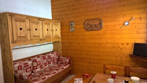 A cozy room with a wooden bench, a small table with a cup, and a television on a wooden shelf.