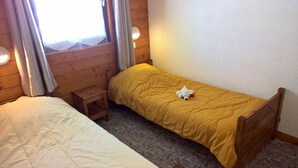 A small, cozy room with two single beds, a wooden nightstand, and a window with curtains.