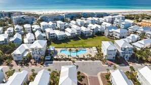 Um resort costeiro com edifícios de vários andares, uma piscina central e vista para a praia.