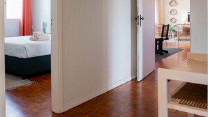 Hotellihuone, jossa on puulattia, valkoisilla lakanoiden peitetty sänky, riippuvalaisin ja näkymä viereiseen ruokailutilaan.