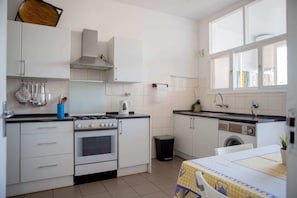 Uma cozinha compacta com armários brancos, fogão, forno e máquina de lavar.