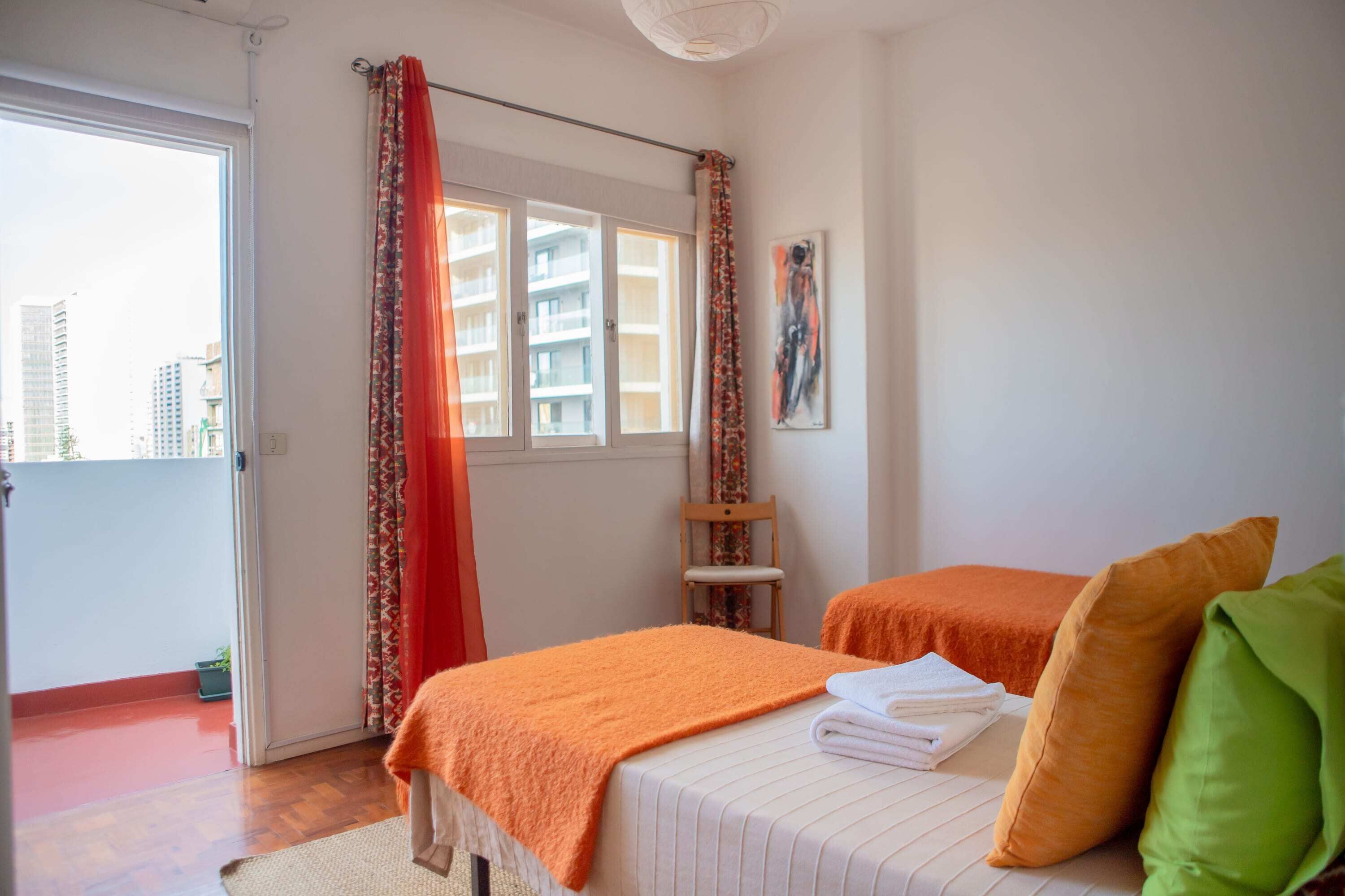 Une chambre avec deux lits, une fenêtre avec des rideaux, une chaise et un tableau accroché au mur.