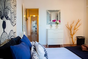 Um quarto com cama, cômoda, espelho e um vaso com flores.