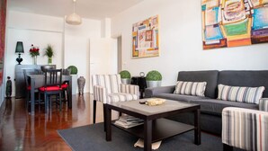 A modern living room with a sofa, striped armchairs, a coffee table, and a dining area with a table and chairs. - Maison Moz - Moldarte (Maputo)