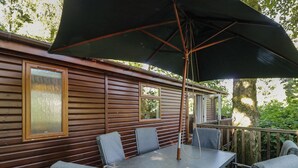 Une terrasse avec une table et des chaises, un parasol et une façade extérieure de style cabane en bois.