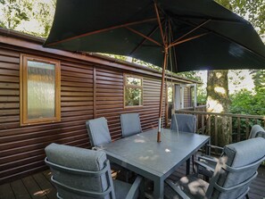 A deck with a table and chairs, an umbrella, and a wooden cabin-style exterior.