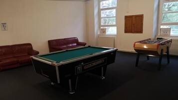 Una mesa de billar en una habitación con un sofá de cuero rojo y una mesa de fútbolín.