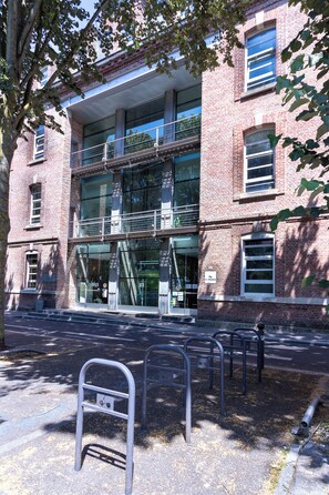 A multi-story brick building with large windows and a metal staircase leading to an upper level. - Auberge de Jeunesse HI Amiens (Amiens)
