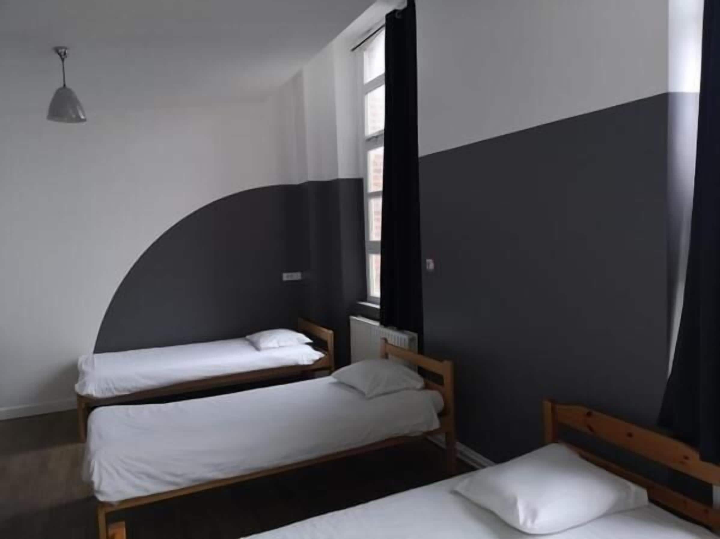 A room with two single beds, a window with curtains, and a hanging light fixture.