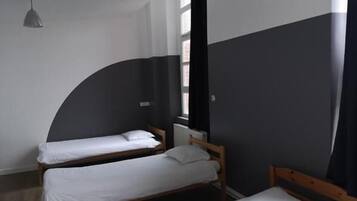 A room with two single beds, a window with curtains, and a hanging light fixture.
