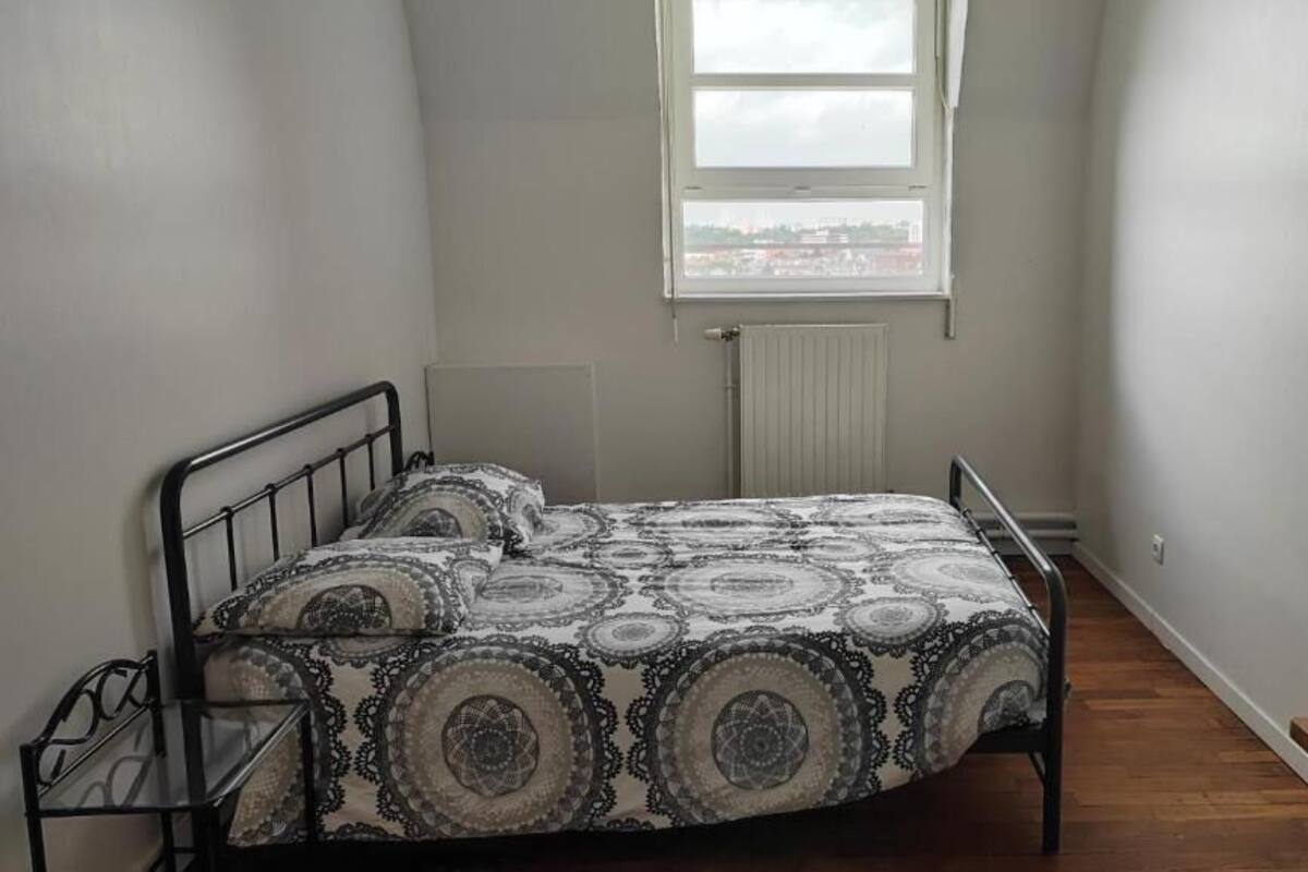 Habitació petita amb un llit individual, un edredó estampat, una finestra amb vista i un radiador a la paret.