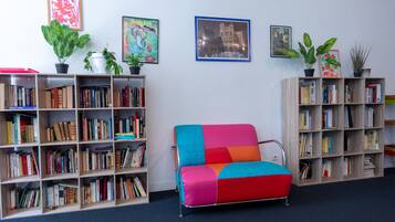 Een kamer met een kleurrijke bank, twee boekenplanken vol boeken en drie potplanten.