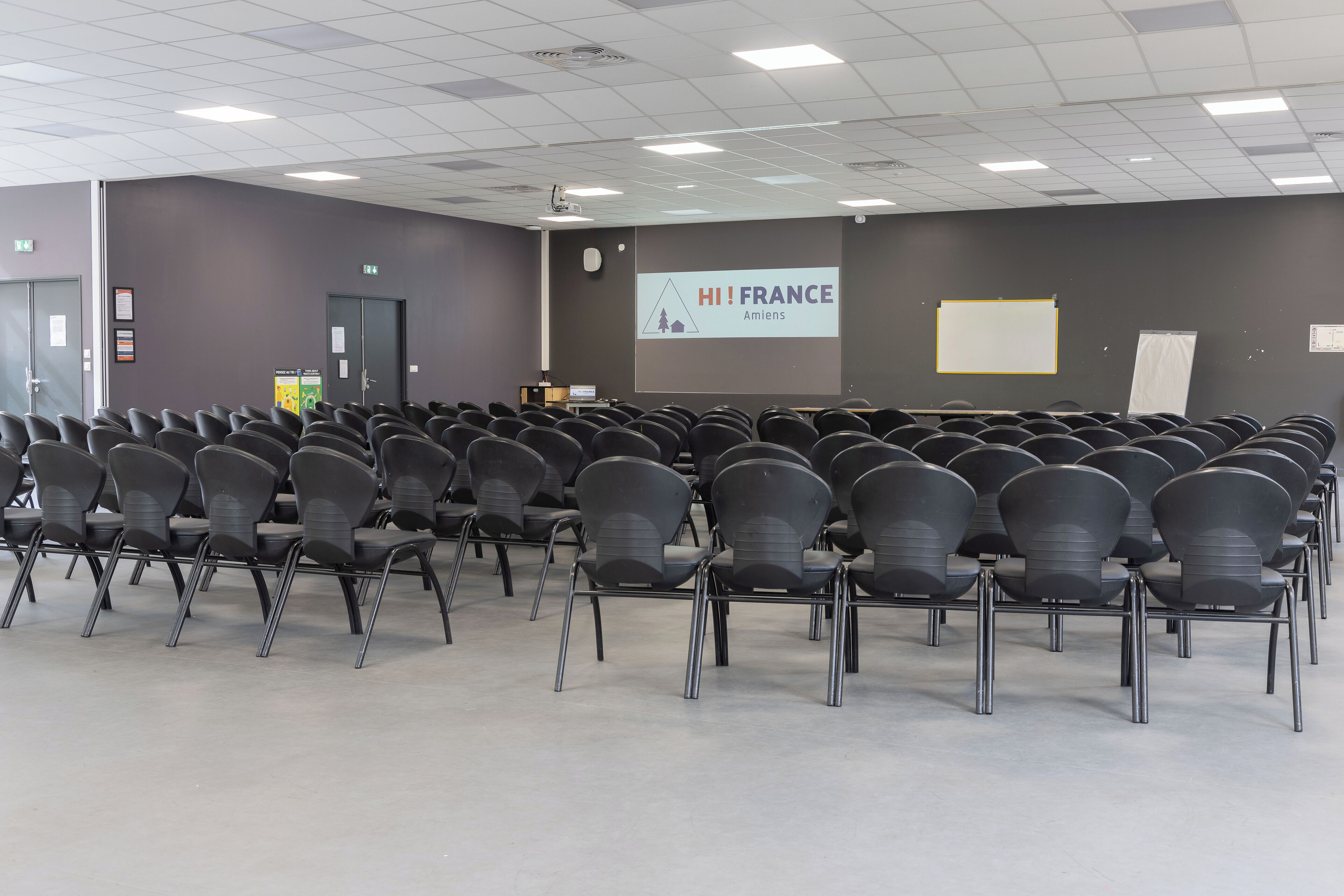 A conference room with rows of chairs, a projector screen, and a presentation titled 'HI! FRANCE'.