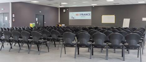 Un salón de conferencias con filas de sillas, una pantalla de proyector y una presentación titulada 'HI! FRANCE'.