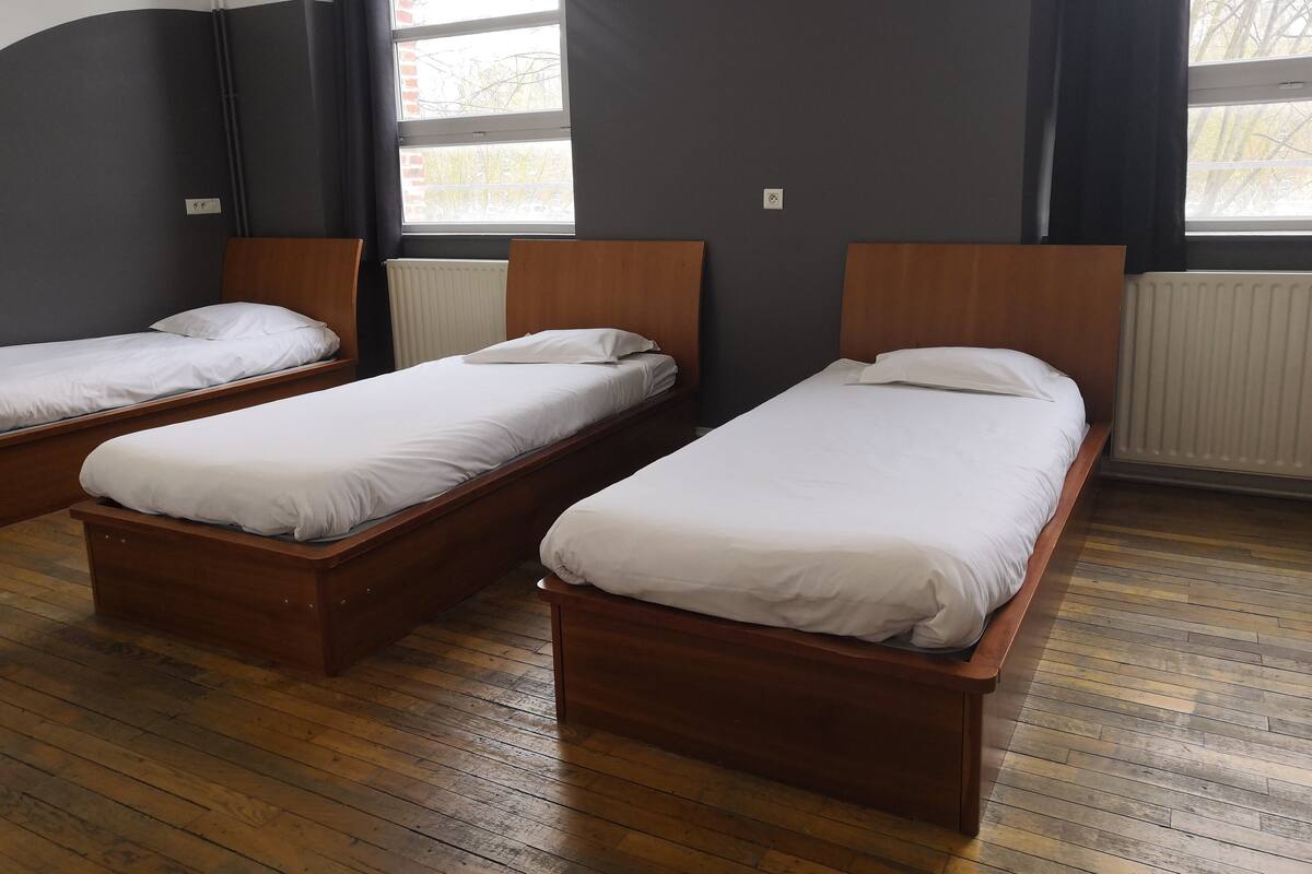 Una habitació amb tres llits de fusta alinear contra una paret amb grans finestres.