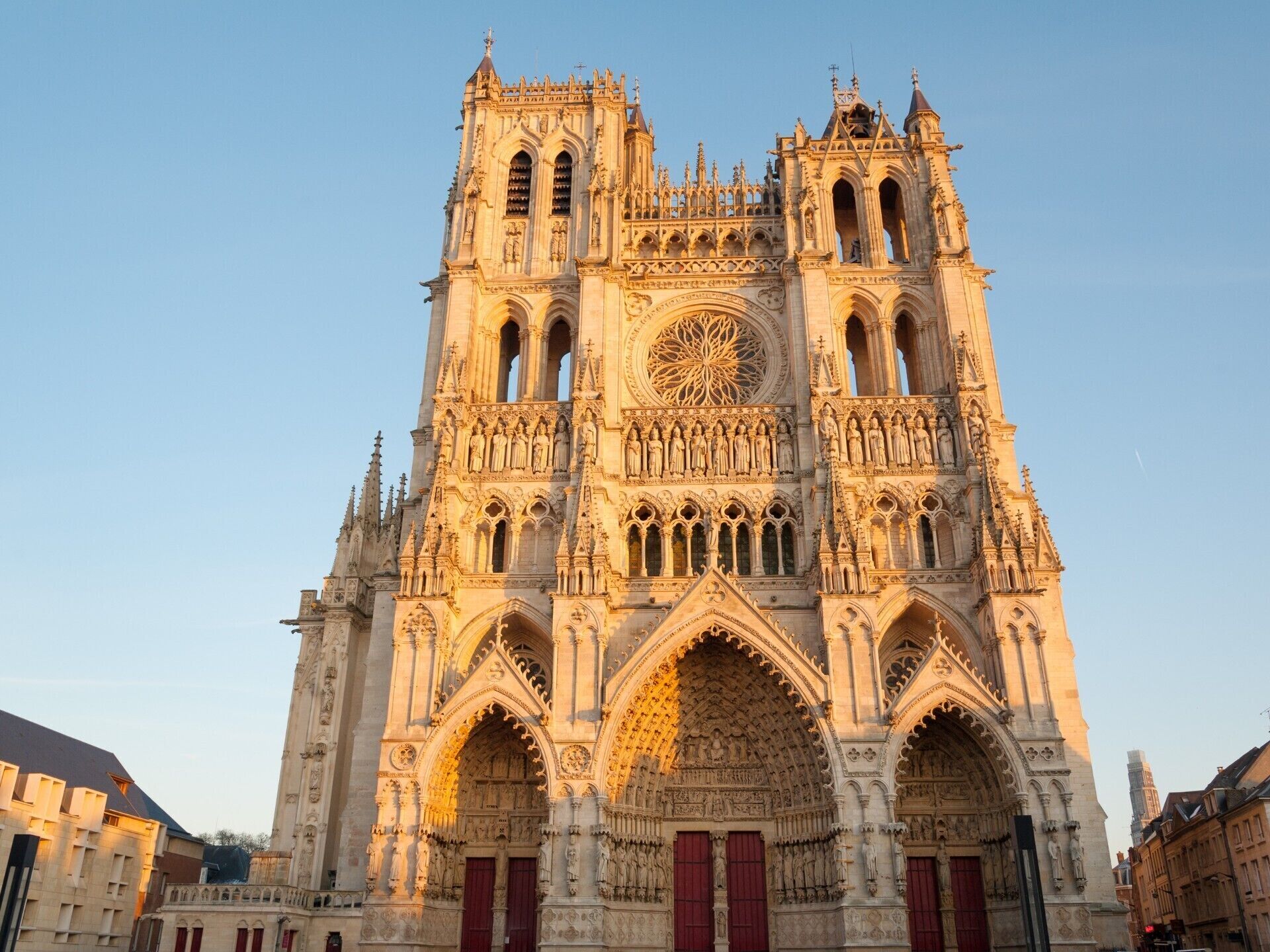 A Gothic cathedral with intricate stone carvings, large rose window, and red doors.