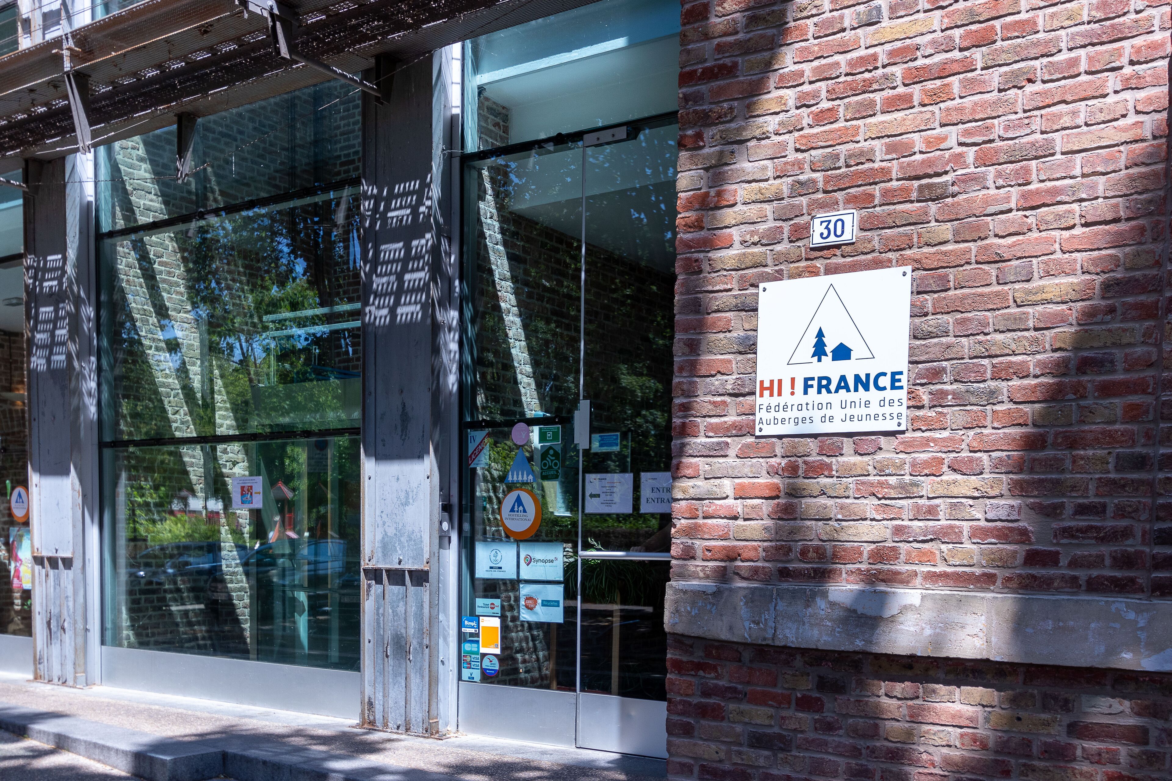Une entrée d’immeuble avec une porte en verre, un mur en briques et une enseigne indiquant qu’il s’agit d’une auberge de jeunesse.