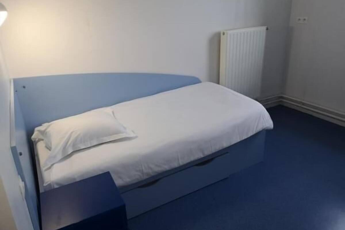 Un llit individual amb matalàss i almoina blanca en una habitació amb parets i terra blaus.