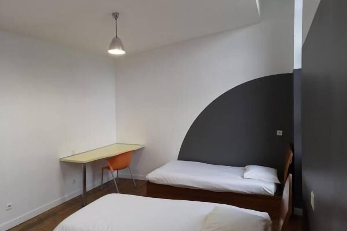 Habitació moderna i petita amb un llit, un escriptori i una cadira.