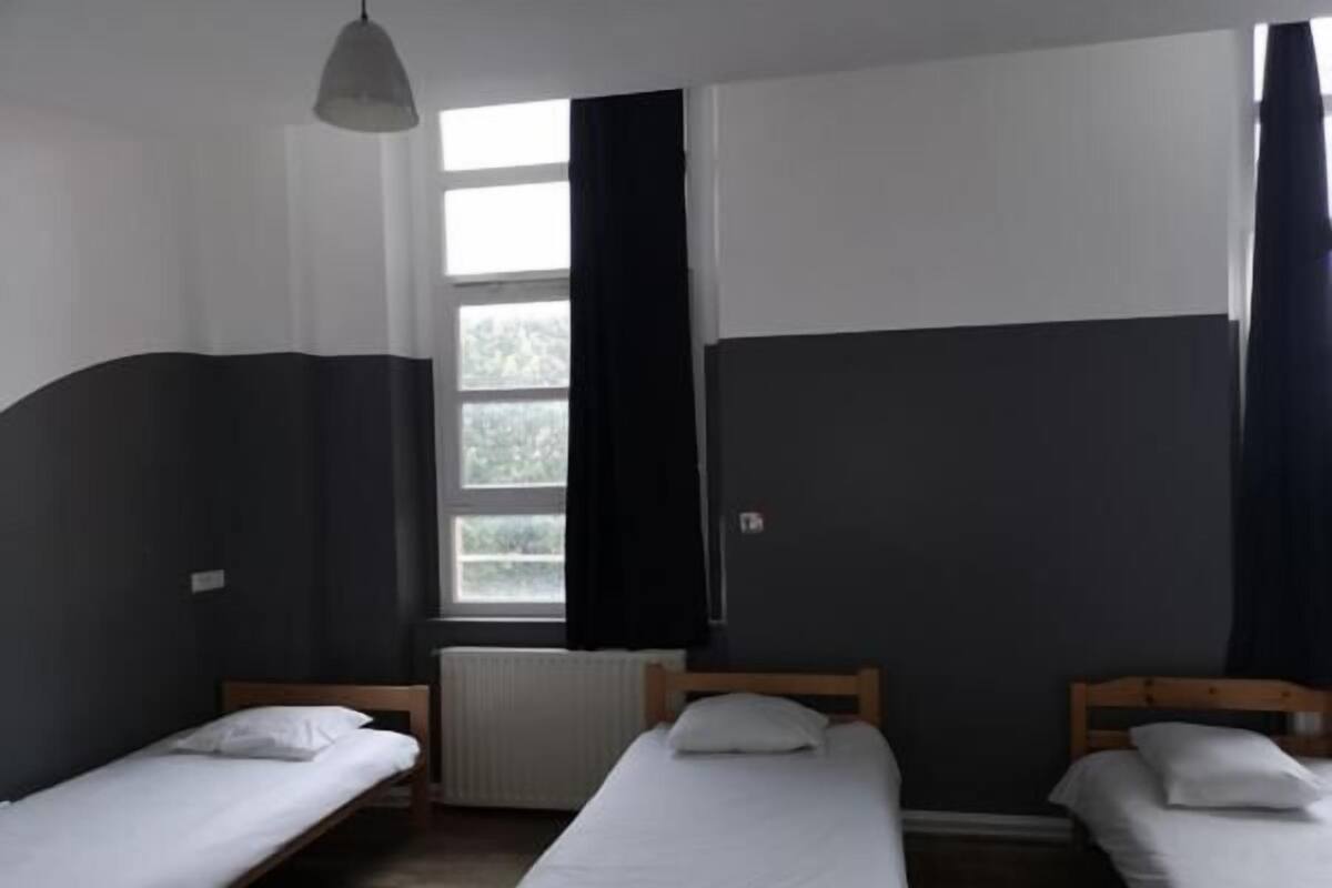 Habitació amb tres llits individuals, un radiador i una finestra amb cortines.