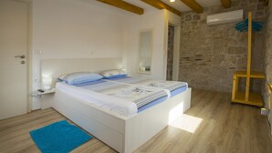 Un dormitorio con una cama, un tapete azul, suelo de madera, pared de piedra y techo con vigas a la vista.
