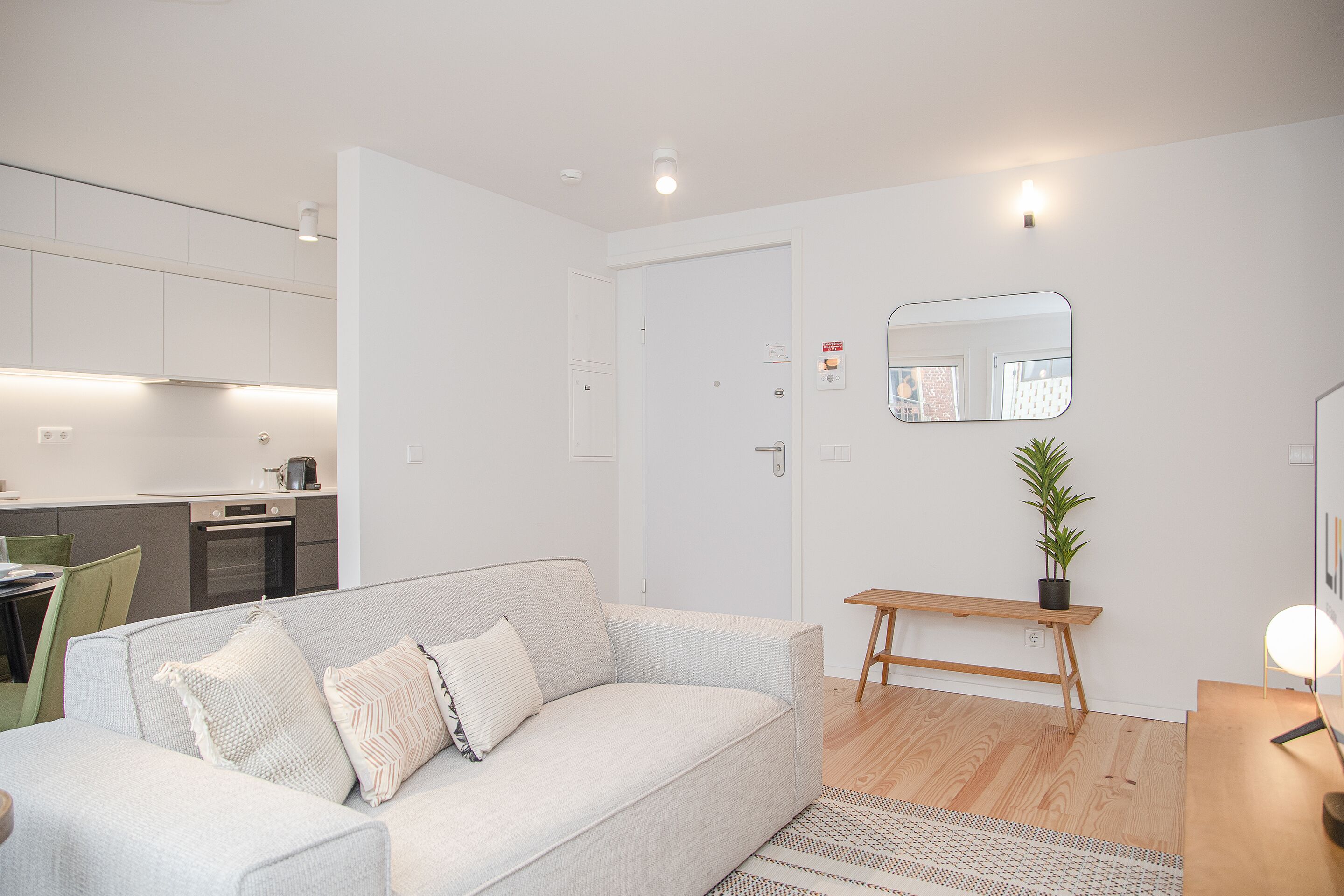 A modern living room with a grey sofa, a wooden side table, and a mirror on the wall.