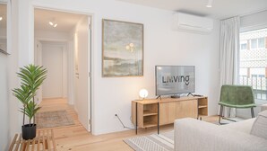 A modern living room with a wooden floor, a green chair, a TV, and a painting on the wall. - Liiiving - Modern & Glam Apartment M (Porto)