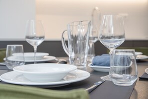 A dining table set with white plates, bowls, and clear glassware, including wine glasses and a pitcher. - Liiiving - Modern & Glam Apartment M (Porto)