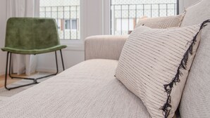 A bedroom with a large bed, a green chair, and two windows with a view of buildings. - Liiiving - Modern & Glam Apartment M (Porto)