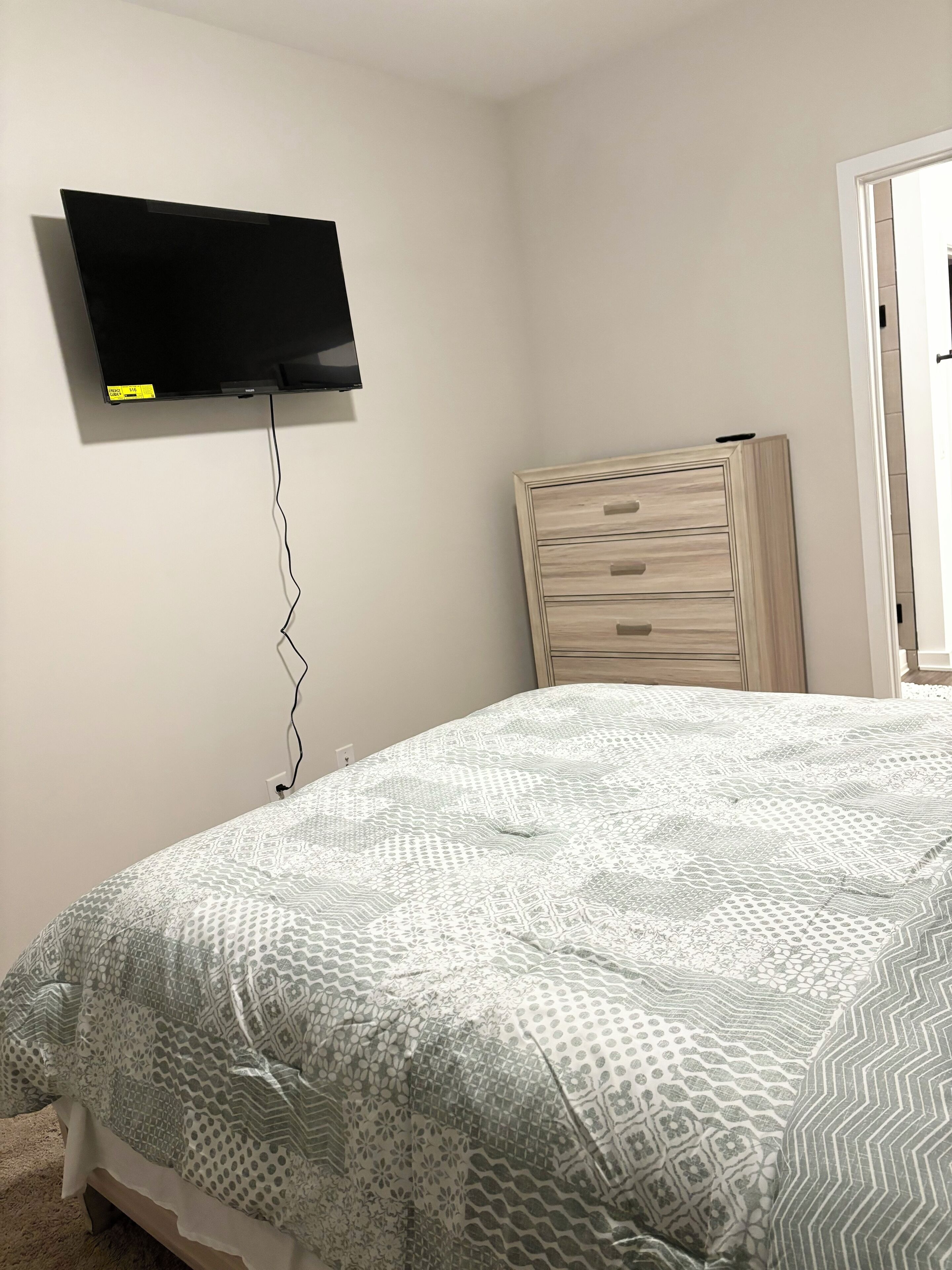 Un dormitorio con una cama, un televisor de pared, un aparador de madera y una puerta.