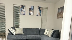 Una sala de estar moderna con un sofá seccional gris, suelo de madera y arte abstracto en la pared.