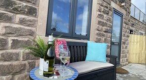 Relax in a serene outdoor space with a stone wall backdrop, a small table, and a comfortable bench.