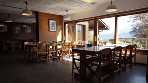 A dining area with wooden tables and chairs, large windows with a view of mountains, and pendant lighting.