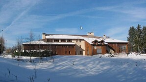 A modern building with a sloped roof, large windows, and a snow-covered landscape.