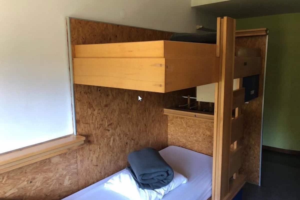 Una cama litera con cabecera de madera, una mesita de noche pequeña y una ventana.