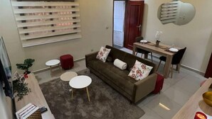 A modern living room with a sofa, coffee table, and dining area. - Appart Cozy Riviera 4 Verdant (Abidjan)