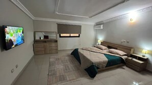 A bedroom with a bed, bedside tables, a TV, a dresser, and a mirror. - Appart Cozy Riviera 4 Verdant (Abidjan)