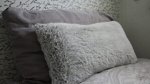 Een bed met een beddeken met patroon en twee kussens, waarvan één pluizig en één glad, tegen een muur met handgeschreven aantekeningen.