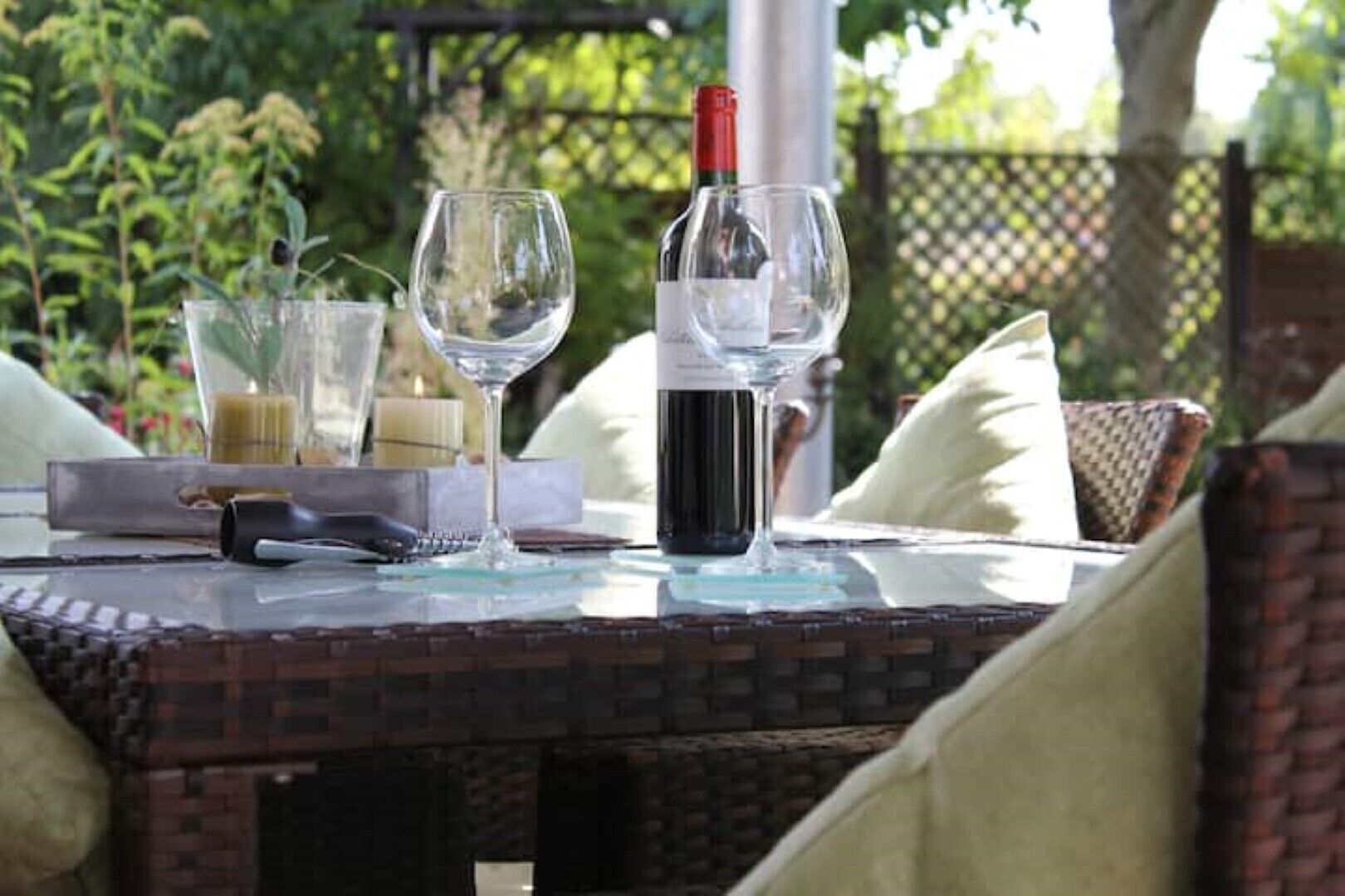 Mesa al aire libre con una botella de vino, dos copas y un control remoto.