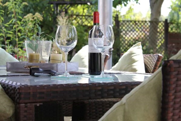 A table set outdoors with a bottle of wine, two glasses, and a remote control.