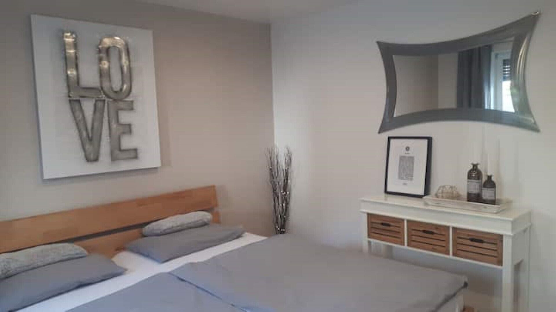Een slaapkamer met een bed, een nachtkastje met spiegel, en een kunstwerk aan de muur met de tekst 'LOVE'.
