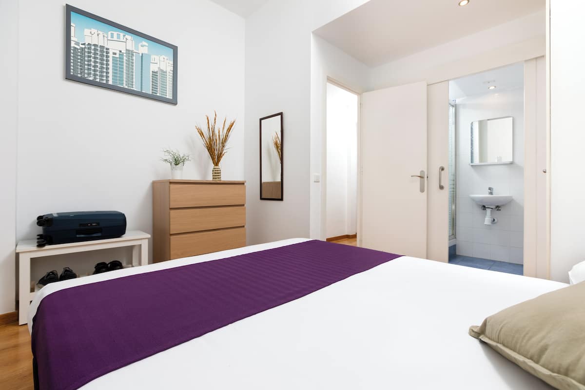 A modern bedroom with a large bed, a dresser, a mirror, and a cityscape painting on the wall.