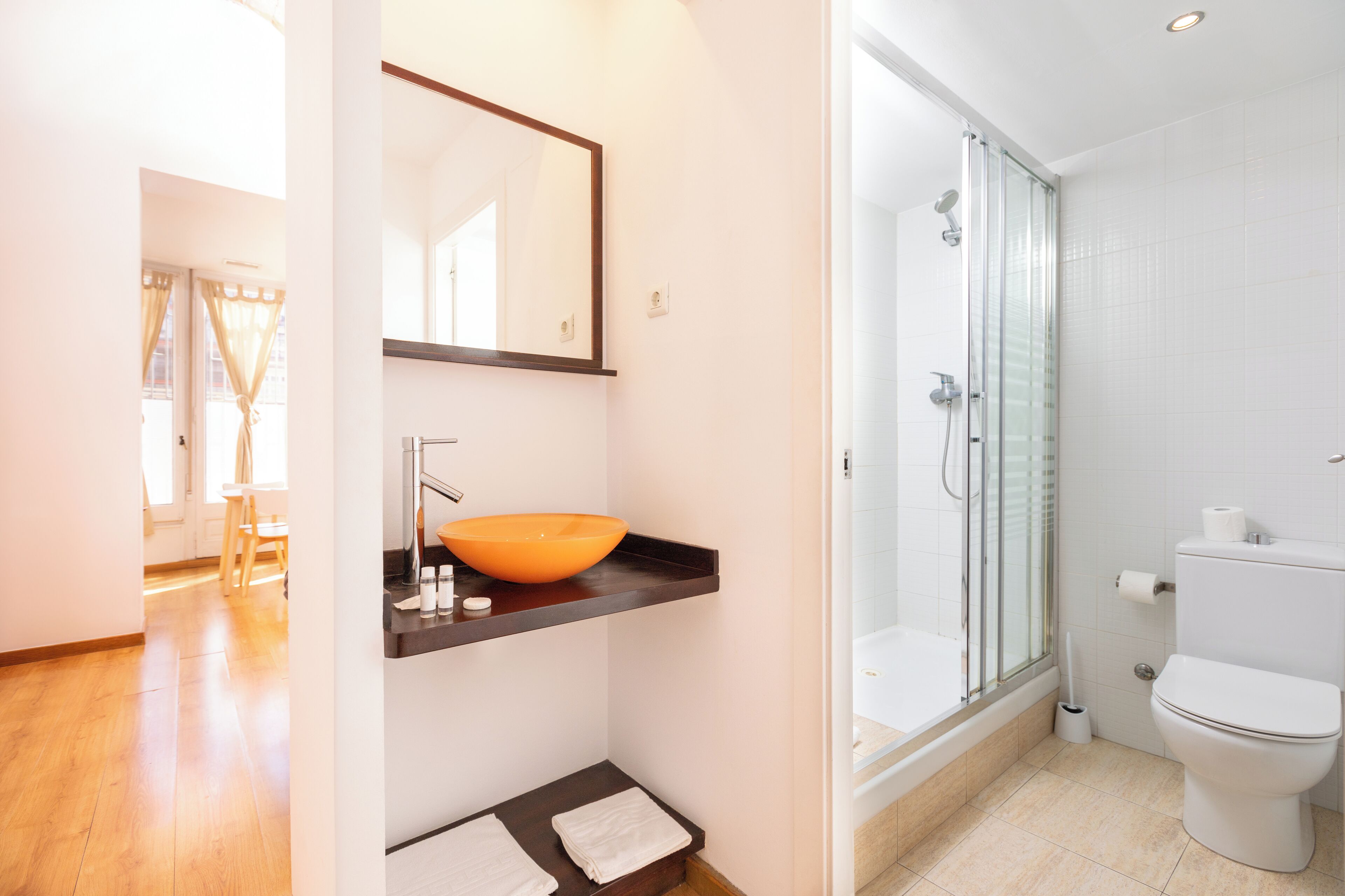 Un bagno moderno con doccia in vetro, vaso bianco e mobile bagno in legno con lavabo arancione.