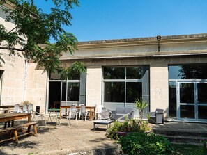 Un espace extérieur aménagé en terrasse, avec des tables et des chaises, de grandes fenêtres et une façade en pierre.