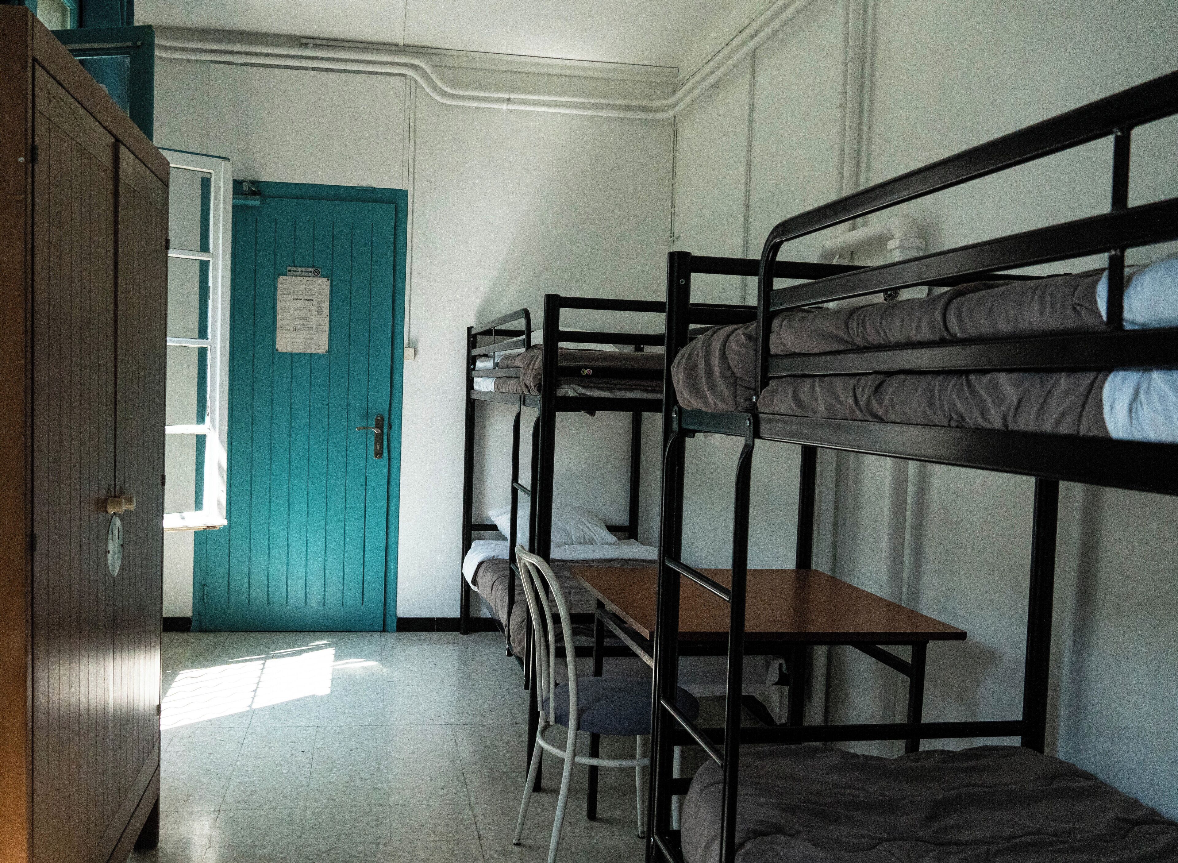 A dormitory room with bunk beds, a desk, and a blue door.